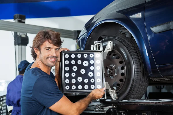 Sorrindo mecânico ajustando a máquina de alinhamento no carro — Fotografia de Stock