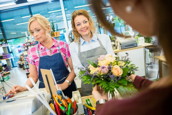 Floristas vendiendo ramo de rosas al cliente en la tienda —  Fotos de Stock