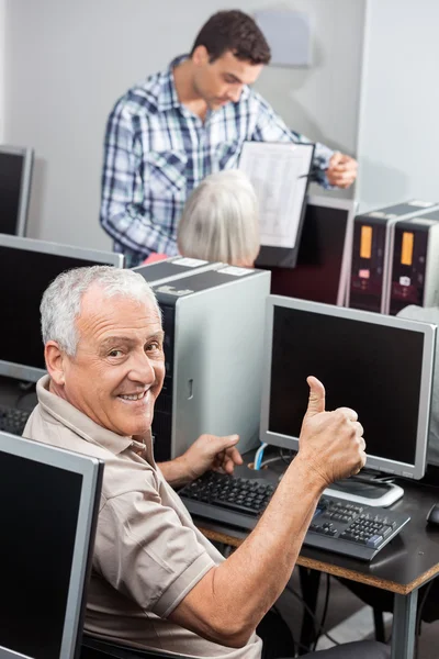 Senior människan gestikulerande tummen upp på datorn skrivbord — Stockfoto