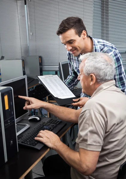 Tutor Klembord te houden terwijl Senior Man assisteren bij het gebruik van Comp — Stockfoto