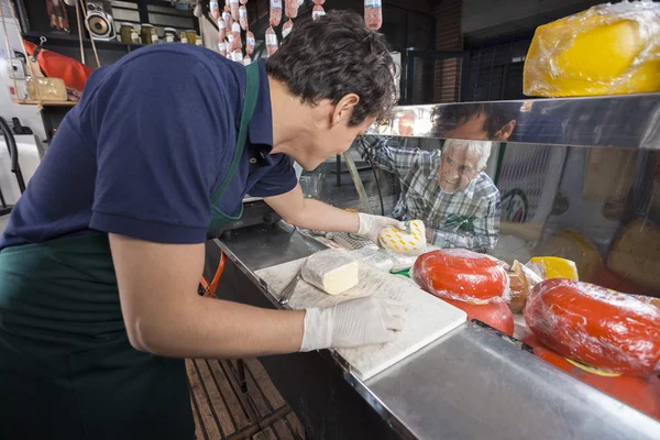 Senior Man kijken werknemer Picking kaas uit vitrinekast — Stockfoto