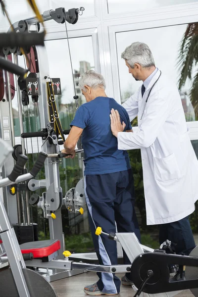 Doctor ayudando al hombre mayor a usar la máquina de ejercicio —  Fotos de Stock