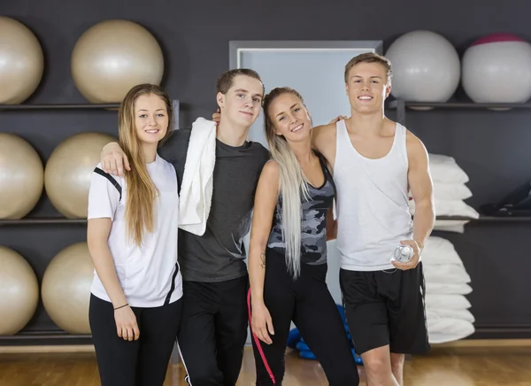 Hombres y mujeres amigos de pie brazos alrededor en el gimnasio — Foto de Stock