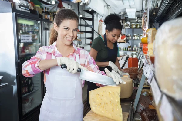 Feliz trabajadora rebanando queso con cuchillo en la tienda —  Fotos de Stock