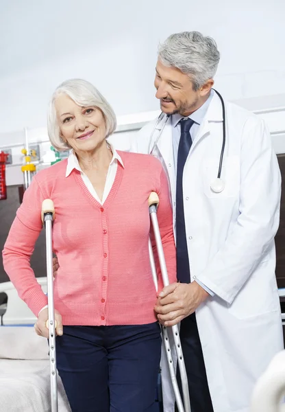 Paciente mayor siendo ayudado por médico con muletas — Foto de Stock