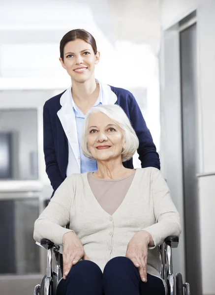 Fisioterapeuta femenina empujando a una mujer mayor en silla de ruedas —  Fotos de Stock