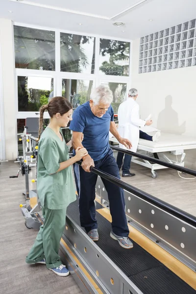 Fyzioterapeut pacienta chodit mezi paralelní Bar v pohotovosti — Stock fotografie