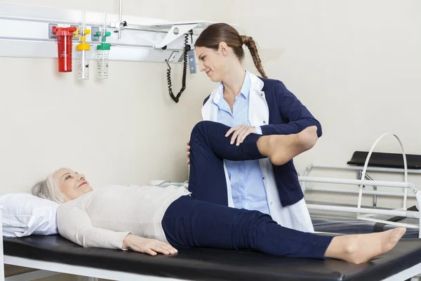 Giovane fisioterapista che aiuta la donna anziana con l'esercizio delle gambe — Foto Stock