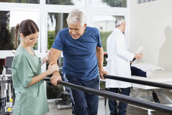 Fisioterapeuta de pie por paciente caminando entre barra paralela —  Fotos de Stock