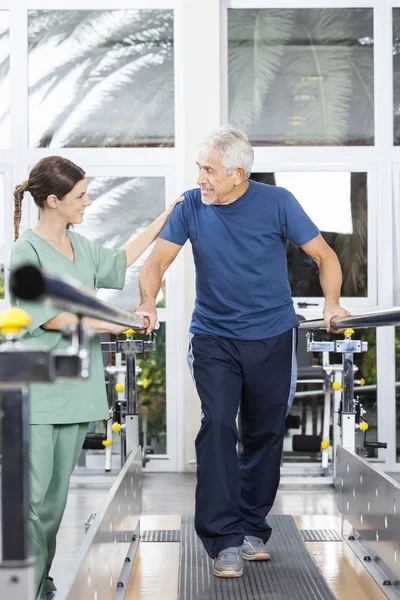 Patiënt kijken naar jonge fysiotherapeut tijdens het wandelen In fitness — Stockfoto
