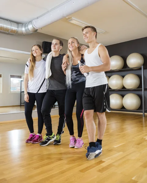 Amici in piedi braccia intorno sul pavimento in legno duro in palestra — Foto Stock