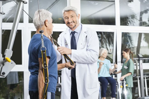 Felice maturo medico assistere anziano uomo con resistenza band — Foto Stock