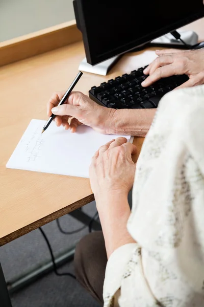 Mujer mayor escribiendo notas en clase de informática — Foto de Stock