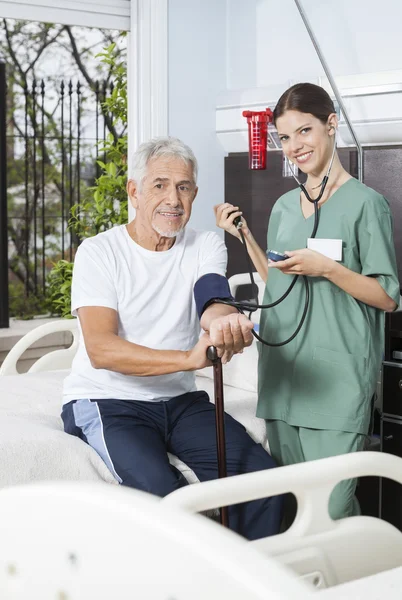 Uśmiechający się pielęgniarka sprawdzania ciśnienia krwi pacjenta w centrum rehabilitacji — Zdjęcie stockowe