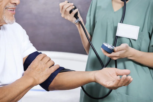 Midsection de la enfermera que comprueba la presión arterial del paciente mayor — Foto de Stock