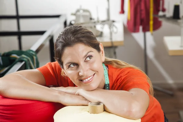 Glimlachend vrouwelijke kleermaker leunend op textiel spoelen — Stockfoto