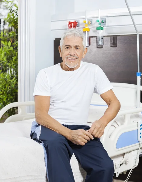 Homem sênior sorridente sentado na cama no centro de reabilitação — Fotografia de Stock