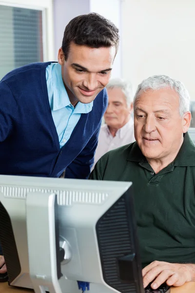 Učitelka pomáhá starší muž v počítačové učebně — Stock fotografie