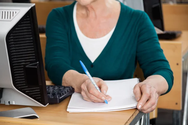 Старшая женщина пишет заметки в компьютерном классе — стоковое фото