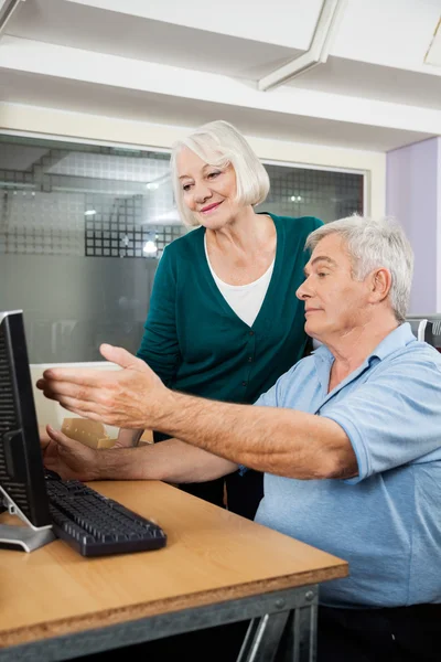 Mujer ayudando a amigo varón en el uso de la computadora en el aula — Foto de Stock