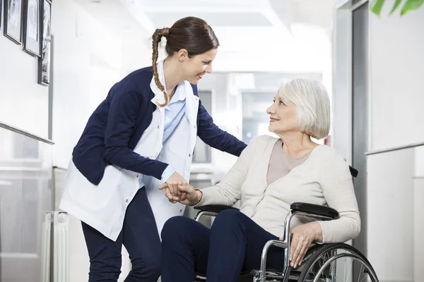 Fisioterapeuta consolando a una mujer mayor sentada en silla de ruedas —  Fotos de Stock