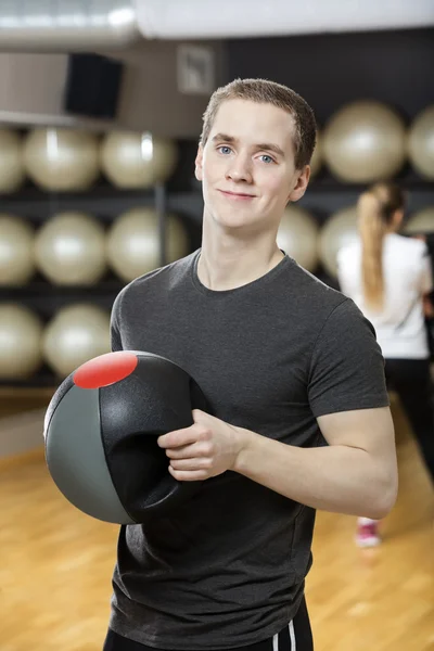Hombre sonriendo mientras sostiene la pelota de medicina en el gimnasio — Foto de Stock