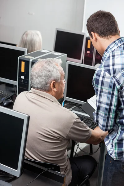 Školitel pomáhající starší muž v používání počítače v učebně — Stock fotografie