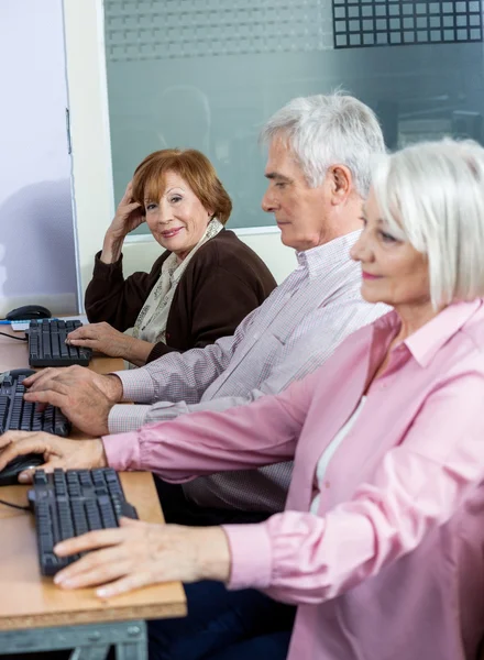 Уверенная пожилая женщина, сидящая с одноклассниками за компьютером — стоковое фото