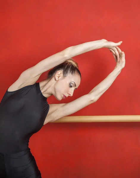 Bailarina estirándose con las manos levantadas contra la pared roja — Foto de Stock