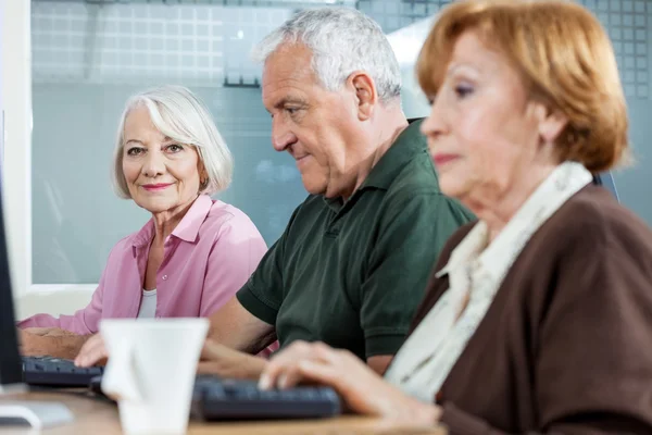 Fiduciosa donna anziana con compagni di classe utilizzando il computer in classe — Foto Stock