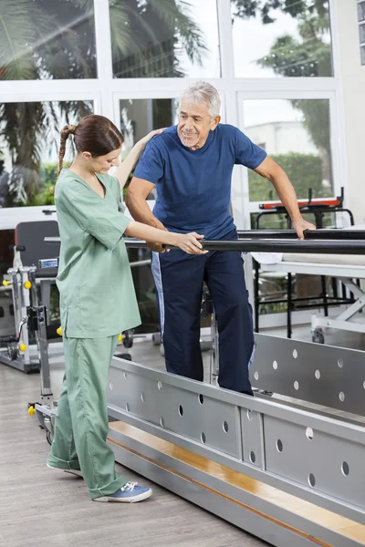 物理治疗师站在高级病人行走之间双杠 — 图库照片