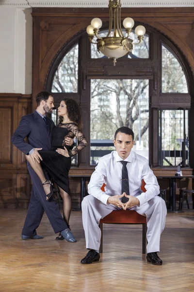 Tancerz Tango pewnie siedzi na krześle, podczas gdy partnerzy Performin — Zdjęcie stockowe