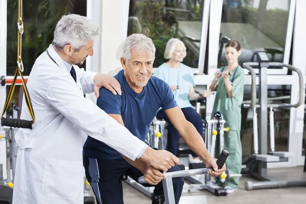 Dokter opdrachtgever Senior Man op hometrainer bij Fitness Center — Stockfoto