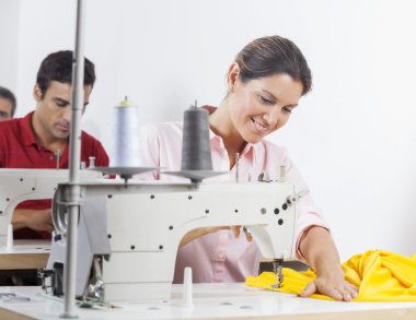 Gülümseyerek terzi fabrikada dikiş makinesi kullanma