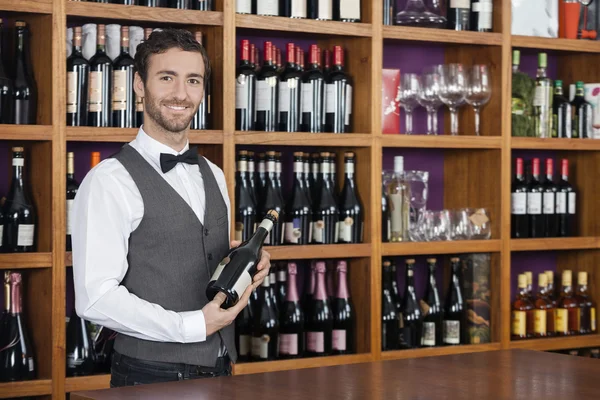 Уверенный бармен держа бутылку красного вина на прилавке — стоковое фото