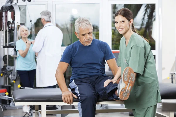 Vrouwelijke verpleegkundige bijstaan van Senior Man In been oefening — Stockfoto