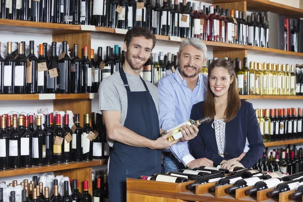 Vendedor segurando garrafa de vinho enquanto está com os clientes — Fotografia de Stock