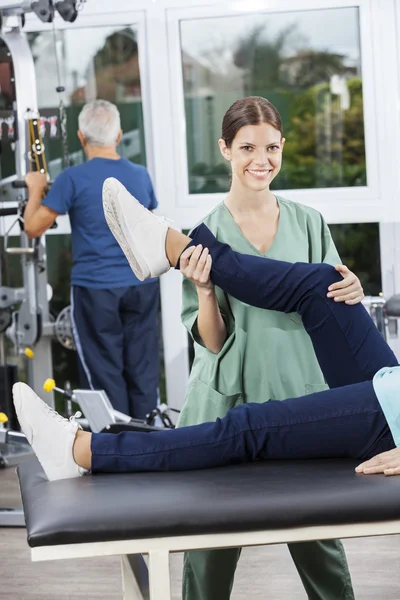 Медсестра ассистирует женщине в упражнении на ногах в реабилитационном фитнес-центре — стоковое фото