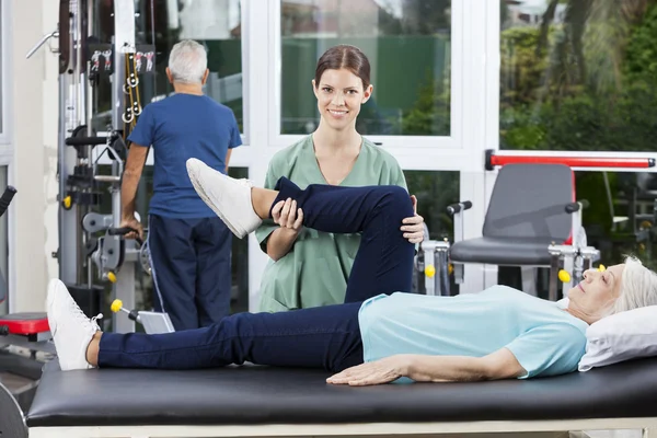 Enfermera asistiendo a una mujer mayor en ejercicio de piernas —  Fotos de Stock