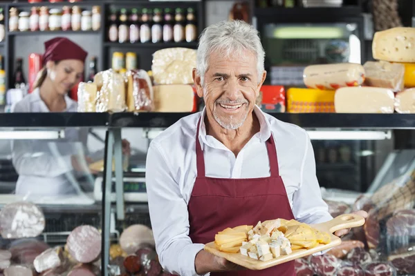 Venditore sorridente che tiene vari formaggi a bordo in negozio — Foto Stock