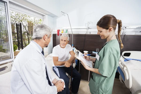 Äldre patienten tittar på läkaren tag sjuksköterska anläggning rapporter — Stockfoto