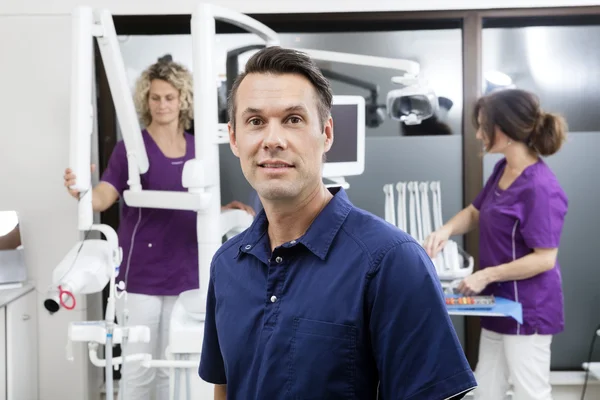 Dentista sonriendo mientras las asistentes femeninas trabajan en la clínica — Foto de Stock