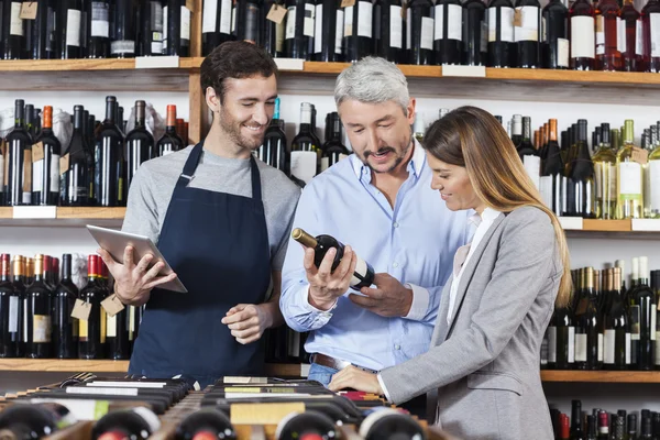 Couple avec bouteille de vin debout par vendeur tenant onglet numérique — Photo