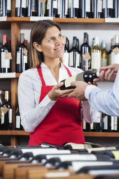 Χαμογελώντας πωλήτρια δίνοντας μπουκάλι κρασί στον πελάτη — Φωτογραφία Αρχείου