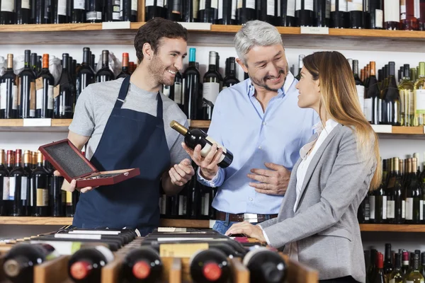 Человек, держащий бутылку вина, стоя с женщиной и продавцом — стоковое фото