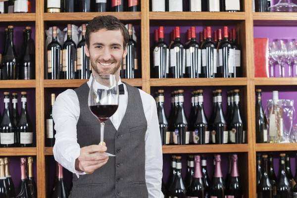 Bartendern erbjuder rött vin glas mot hyllor — Stockfoto