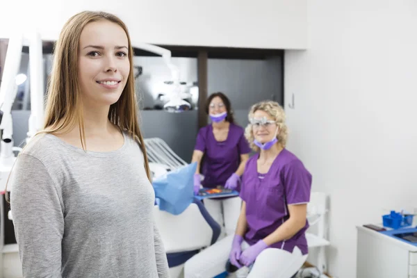 Sonriente paciente femenina con dentistas trabajando en segundo plano —  Fotos de Stock