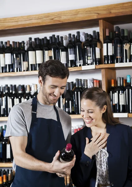 Vendedor mostrando botella de vino a cliente hembra feliz — Foto de Stock