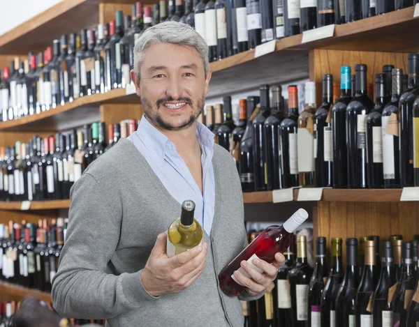 Клиент держит бутылки красного и белого вина в магазине — стоковое фото