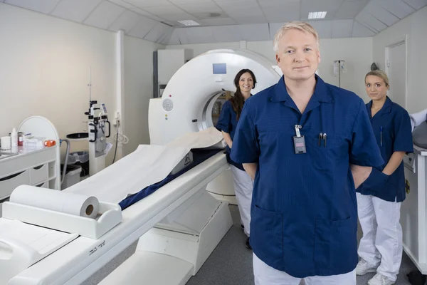 Уверенный в себе мужчина-врач с коллегами, стоящими у аппарата МРТ — стоковое фото